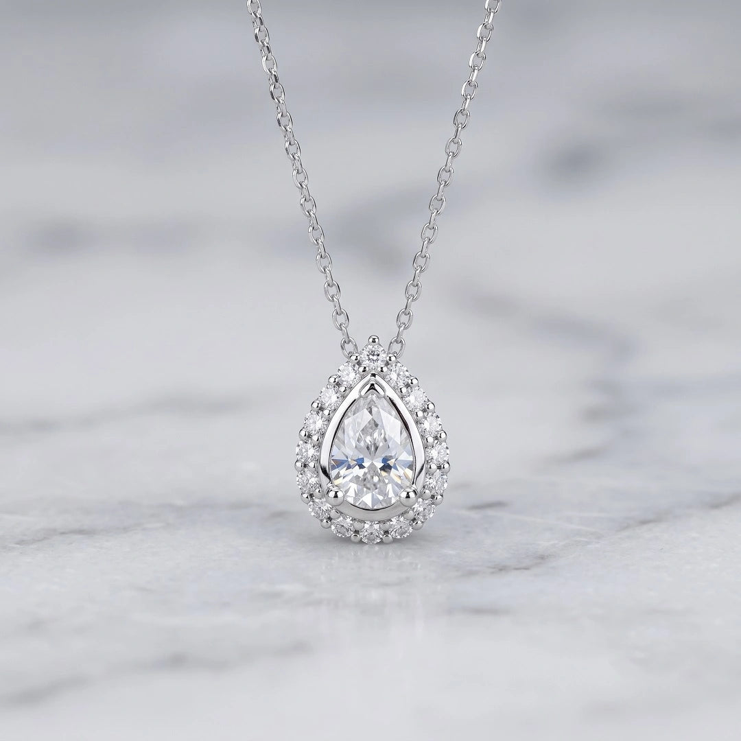 Halo pear shaped moissanite pendant necklace in white gold on white marble background